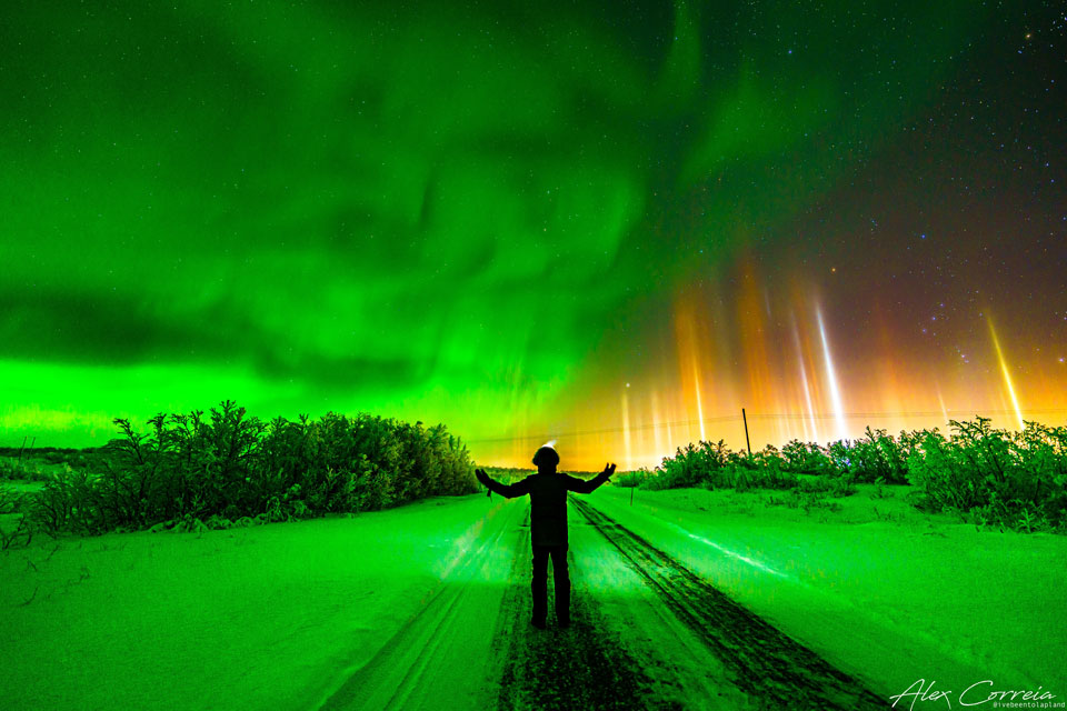 Zdjęcie pokazuje fotografa stojącego pod nocnym niebem z zieloną
zorzą polarną po lewej i barwnymi słupami świetlnymi po prawej.
Zobacz opis. Po kliknięciu obrazka załaduje się wersja
 o największej dostępnej rozdzielczości.