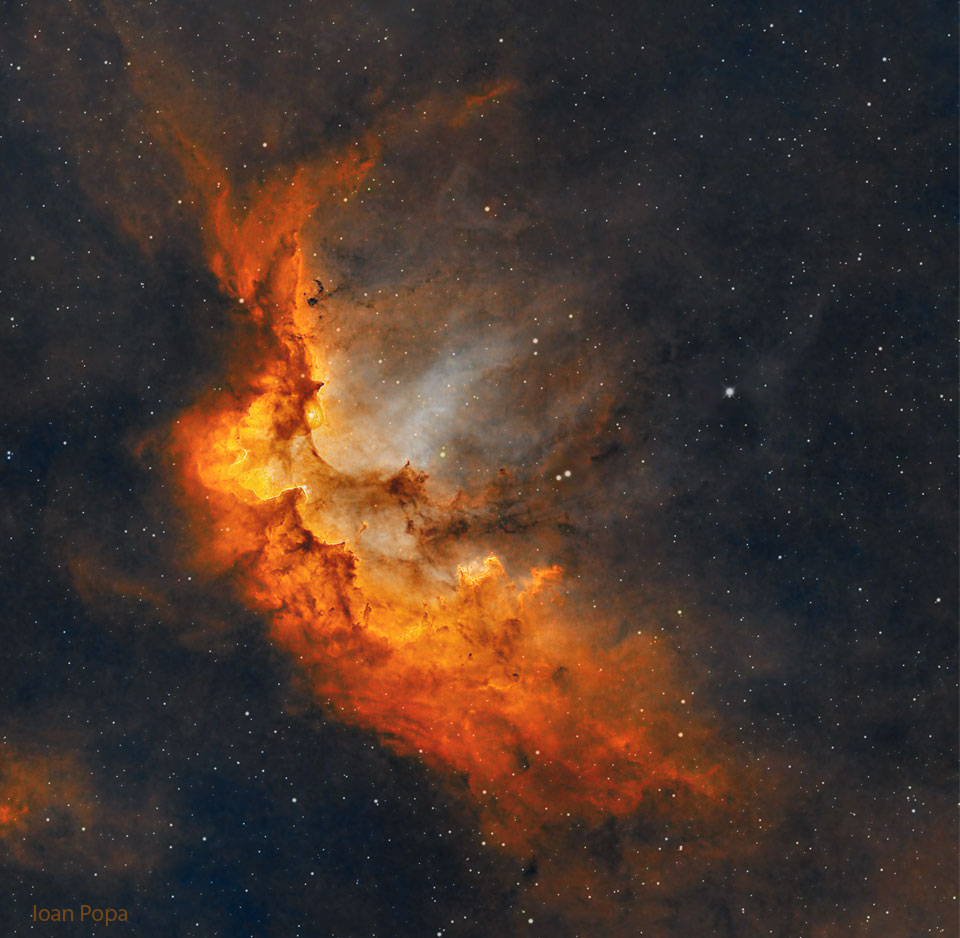 Opisywane zdjęcie pokazuje świecącą na czerwono
Mgławicę Czarodziej z gazem i słupami pyłu na rozgwieżdżonym tle.
Zobacz opis. Po kliknięciu obrazka załaduje się wersja
 o największej dostępnej rozdzielczości.