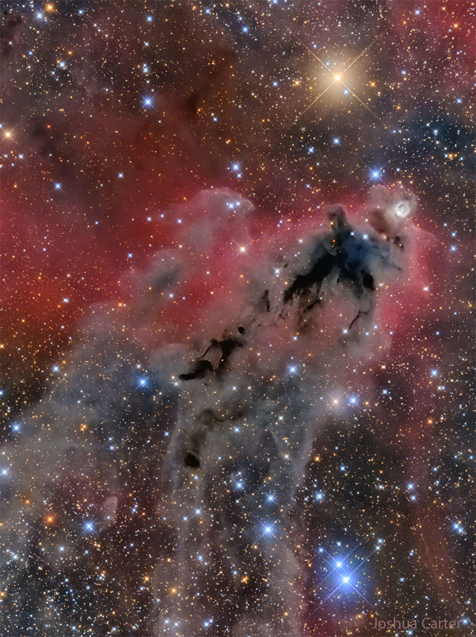 Zdjęcie złowrogiej ciemnej mgławicy na tle świecącego na czerwono gazu
oraz wiele jasnych i barwnych gwiazd. Zobacz opis. Po kliknięciu obrazka załaduje się wersja
 o największej dostępnej rozdzielczości.