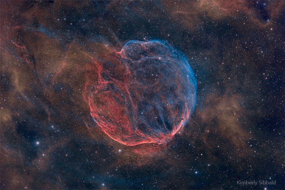 Niemal sferyczna, choć włóknista, niebiesko-czerwona mgławica prezentuje się na tle gwiazd. Więcej szczegółowych informacji w opisie poniżej.