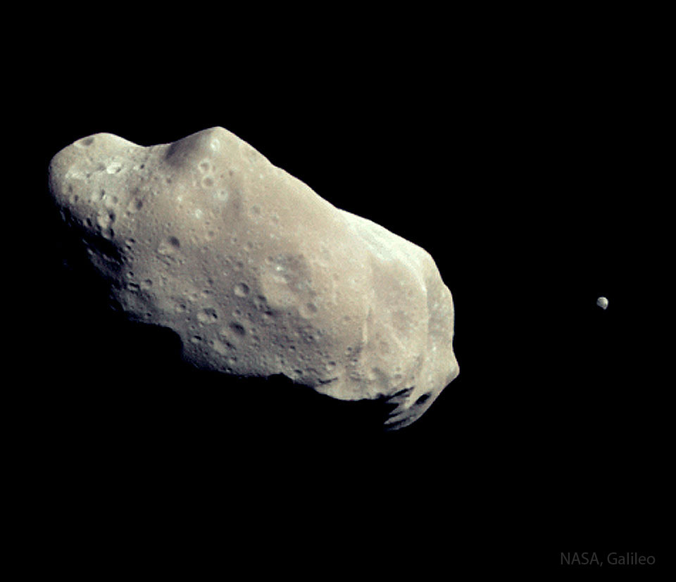 Pokazano parę planetoid: większą, wydłużoną i pokraterowaną
planetoidę po lewej oraz znacznie mniejszą daleko po prawej.
Zobacz opis. Po kliknięciu obrazka załaduje się wersja
 o największej dostępnej rozdzielczości.