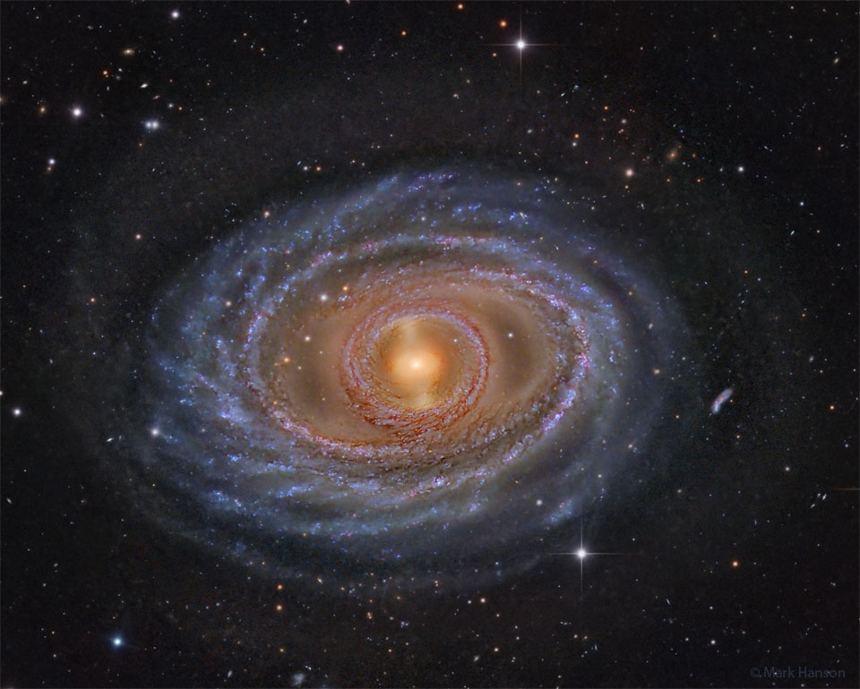 Na zdjęciu pokazano galaktykę spiralną z żółtym centrum,
błękitnymi pierścieniami i ramionami spiralnymi oraz ciemnym
brązowym i czerwonym pyłem. Otaczające ją ciemne pole składa się
zarówno z lokalnych gwiazd, jak i odległych galaktyk.
Zobacz opis. Po kliknięciu obrazka załaduje się wersja o największej dostępnej rozdzielczości.