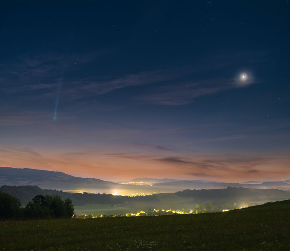 A scenic and hilly landscape is shown just before sunrise. 
On the left is Comet Nishimura near the horizon with a long tail
fading off toward the top of the frame. On the right is a bright spot
that is Venus. The sunrise sky is dark blue at the top but morphs
into tan at the horizon, while the foreground hills are green.
Więcej szczegółowych informacji w opisie poniżej.