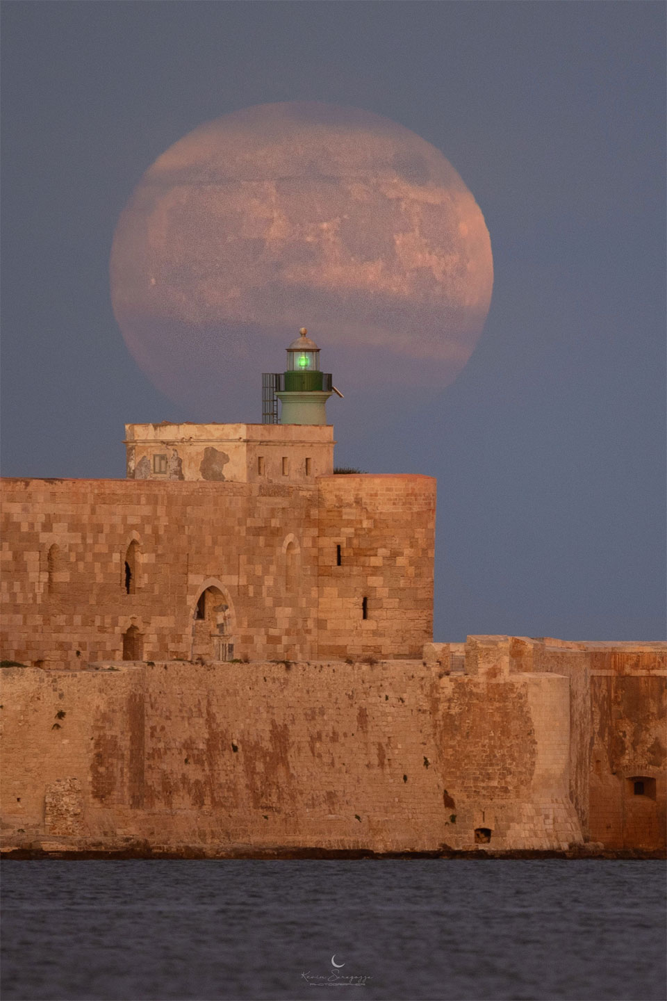 A large Moon is seen behind a historic stone structure. 
Więcej szczegółowych informacji w opisie poniżej.