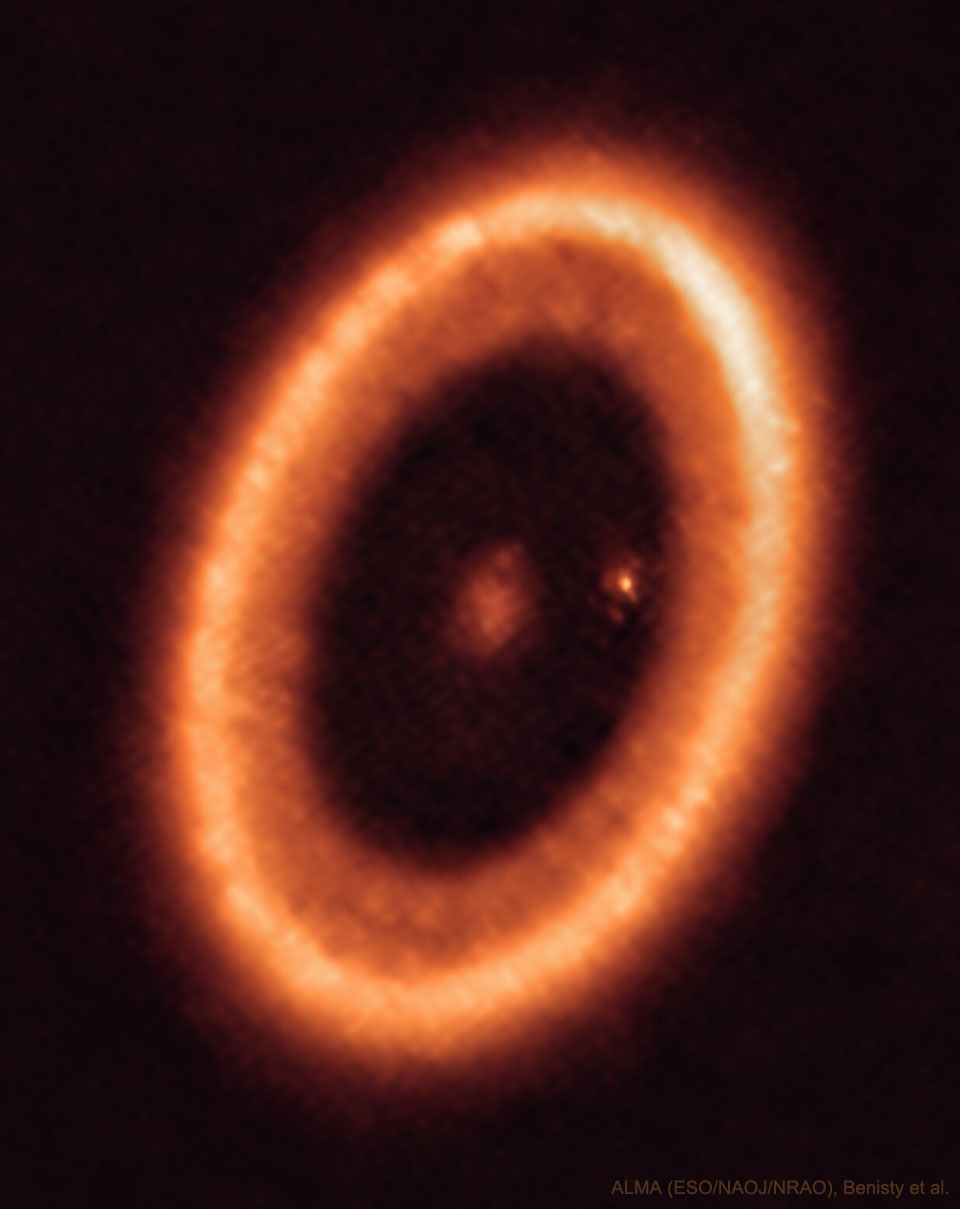 An orange elliptical ring is shown that is a disk of
gas and dust around the star PDS 70. In the center of the disk
is a fuzzy spot and near the inner right edge of the disk is
another fuzzy spot. 
Więcej szczegółowych informacji w opisie poniżej.