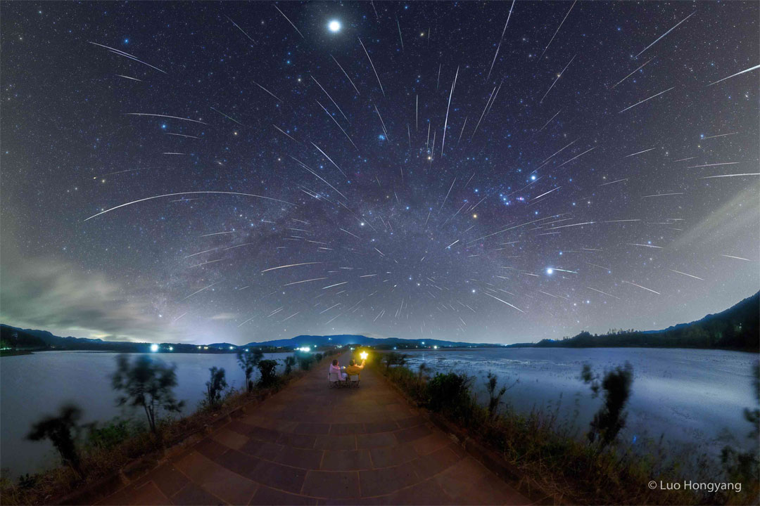 Na zdjęciu widać dwoje ludzi patrzących na ciemne, wypełnione gwiazdami niebo, które przecinają również 
liczne ślady meteorów roju Geminidów.
Więcej szczegółowych informacji w opisie poniżej.