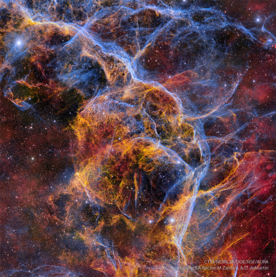 Złożone wielobarwne włókna przecinają zdjęcie na tle
rozgwieżdżonego pola gwiazd. Niektóre obszary mają rozmytą
czerwono-pomarańczową poświatę. 
Zobacz opis. Po kliknięciu obrazka załaduje się wersja
 o największej dostępnej rozdzielczości.