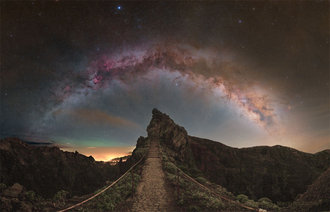 A star filled sky shows the arch of the central band of
our Milky Way galaxy across the top of the image. In the foreground
is a rocky landscape with a hill ahead and a pathway that leads
to stairs up that hill.
Więcej szczegółowych informacji w opisie poniżej.