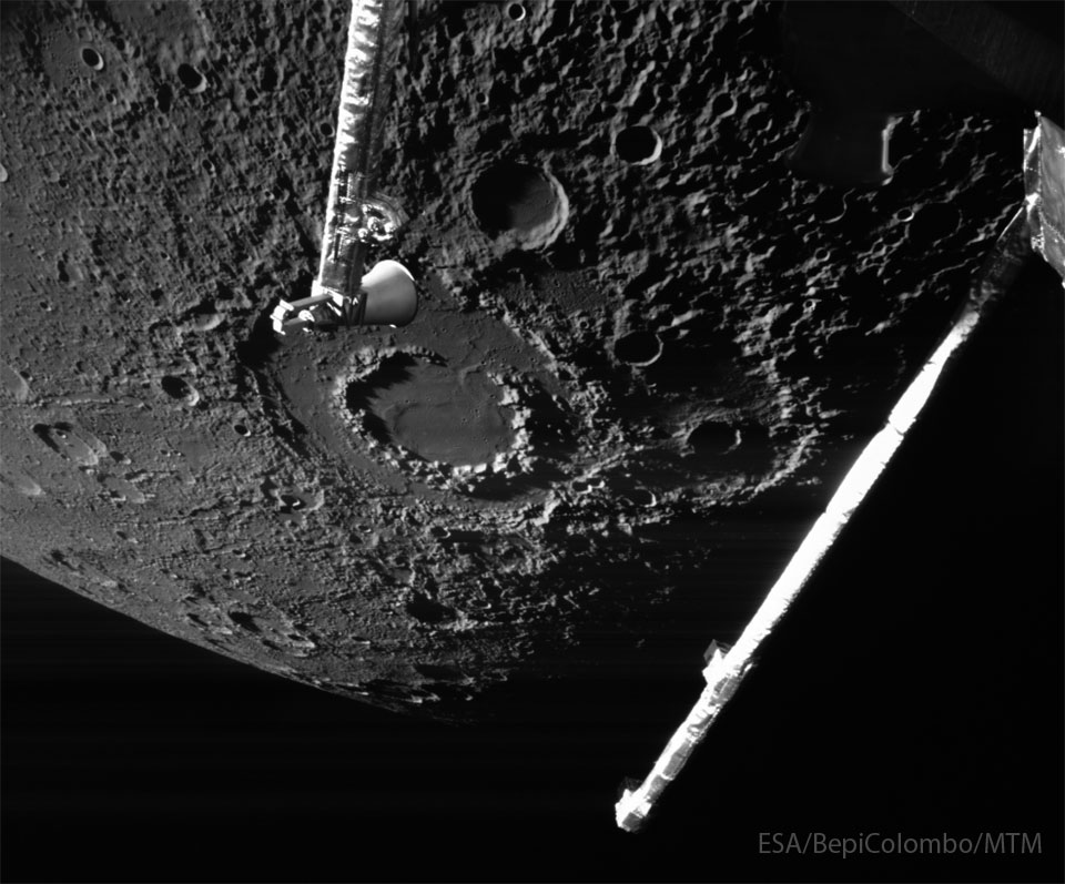 The cratered surface of a large body is shown: Mercury.
The largest feature visible is a large impact crater with two
rings, near the image center. Arms from the BepiColumbo 
spacecraft that took the image are seen extending into the 
image from the top and the right. 
Więcej szczegółowych informacji w opisie poniżej.