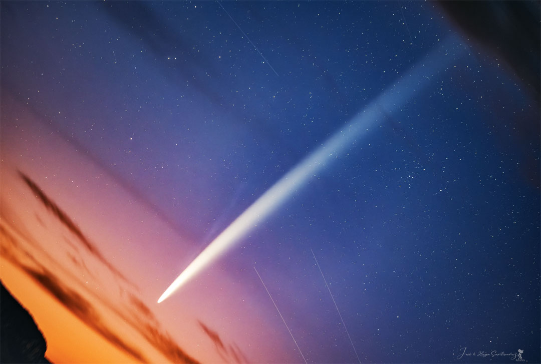 A starry sky is pictured with a long bright streak running
diagonally from the lower left to the upper right. The lower
left part of the sky sky orange sprinkled with a few dark
clouds. 
Więcej szczegółowych informacji w opisie poniżej.