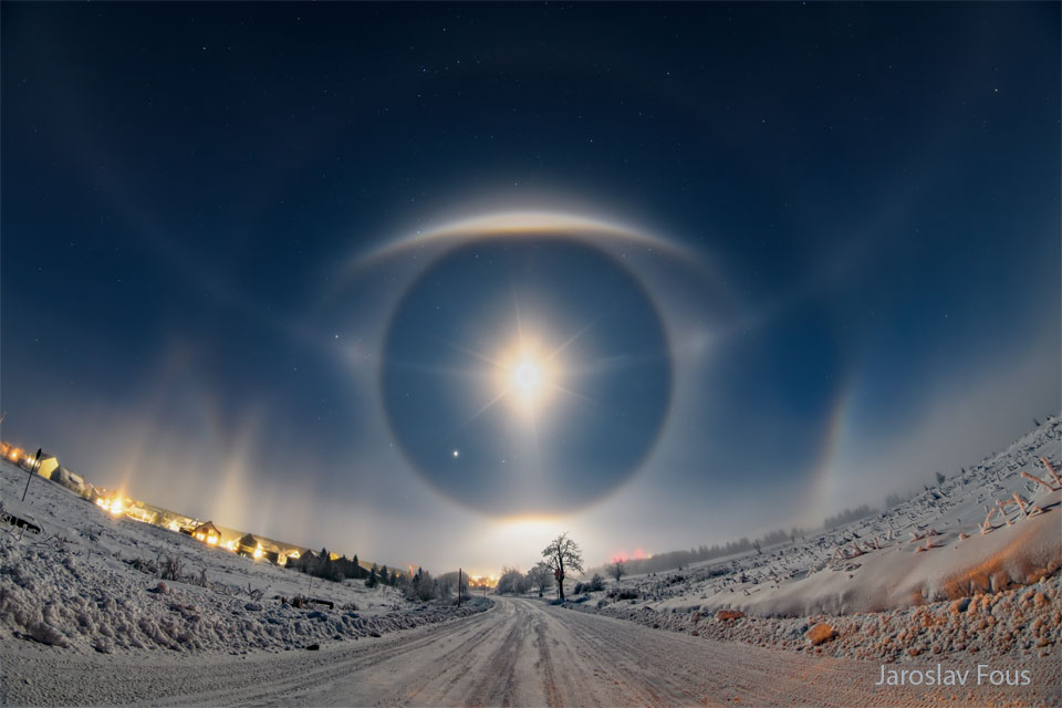 A snow covered road goes up a hill to a sky filled with
stars. Arcs and halos in the sky ahead appear similar to a giant
eye. 
Więcej szczegółowych informacji w opisie poniżej.