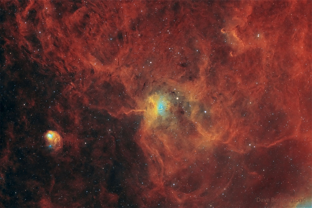 A star field has a red diffuse glow on the right-hand side.
Distinct nebulas appear in the center and on the lower left. 
Więcej szczegółowych informacji w opisie poniżej.