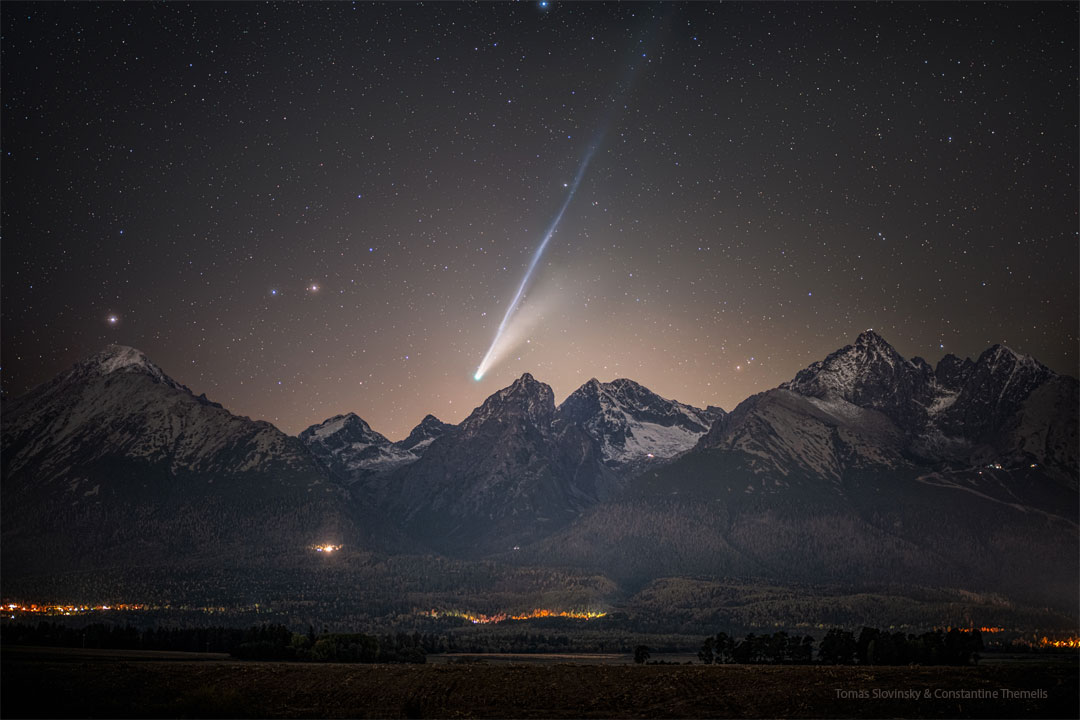 A mountain range is shown in the foreground with a
bright comet visible above it. The comet shows tails
that are long and bright with the longer tail appearing
light blue. 
Więcej szczegółowych informacji w opisie poniżej.