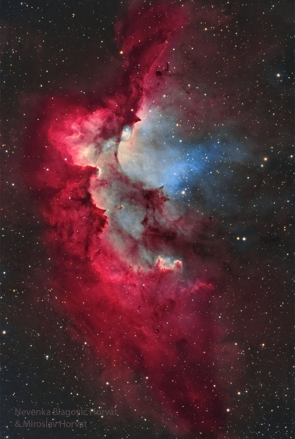 A starfield is shown surrounding a bright gaseous 
nebula in red with bits of white and blue. Pillars of 
dust and gas appear around the interior of the nebula
pointing to energetic stars in a cluster in the nebula. 
Więcej szczegółowych informacji w opisie poniżej.