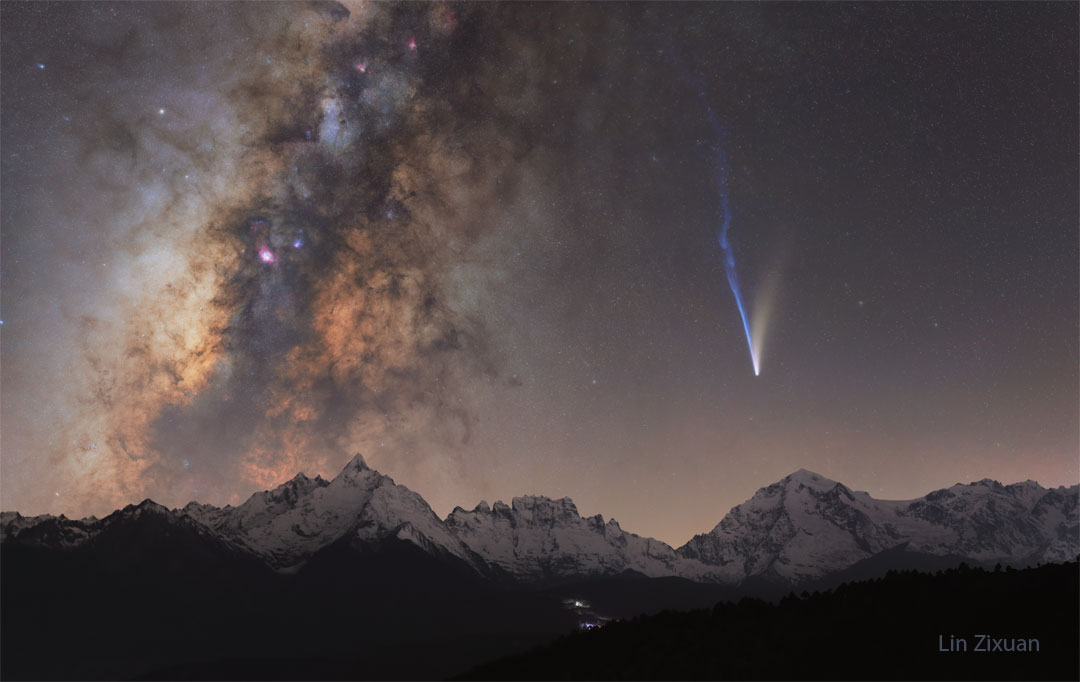 A night skyscape is shown over snowcapped mountains.
On the left is the band of the Milky Way Galaxy, while
on the right is a bright comet with two tails -- a white
tail going up and trailing to the right and a longer blue
tail going up and trailing off to the left. 
Więcej szczegółowych informacji w opisie poniżej.