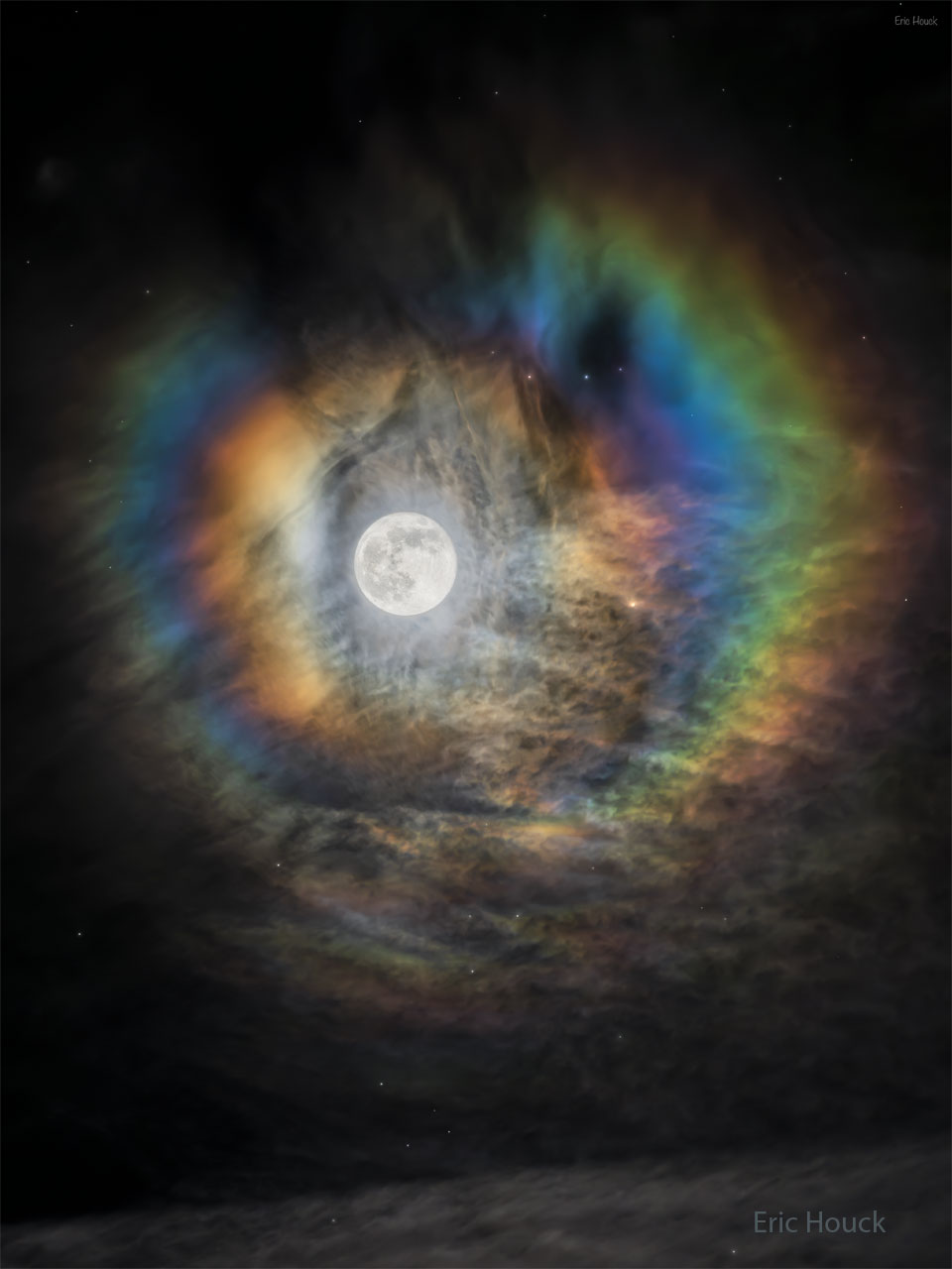 The Moon is pictured in the center. ARound the Moon are
colorful rings. The rings are nearly circular but have gaps.
This but structured clouds are seen around the scene and
at the bottom of the frame. 
Więcej szczegółowych informacji w opisie poniżej.