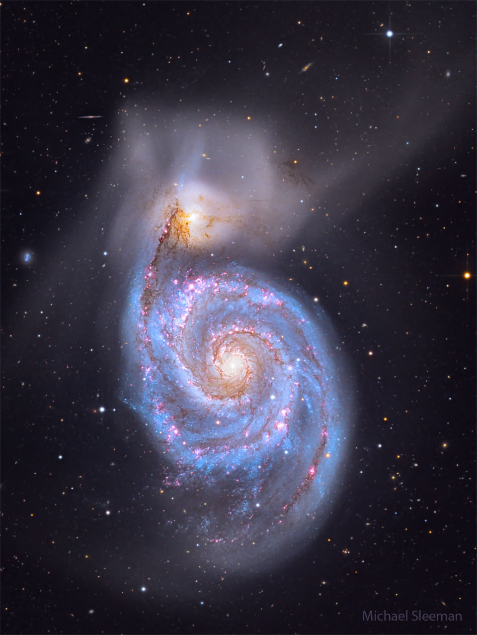 A big spiral galaxy fills the frame, complete with blue
spiral arms dotted with red dust and nebulas. Above the 
spiral galaxy is another more diffuse galaxy that has
faint wisps extending in many directions. 
Więcej szczegółowych informacji w opisie poniżej.