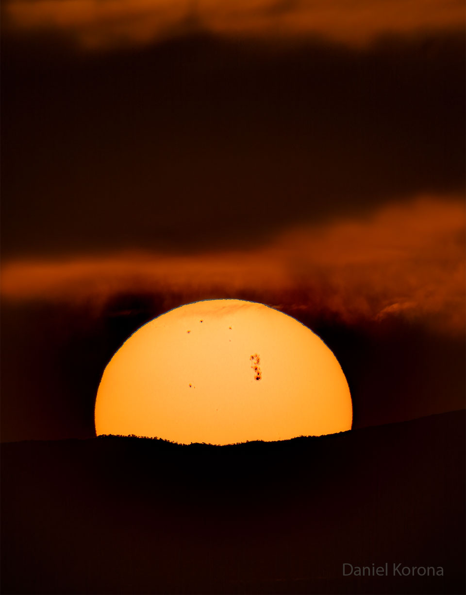 Most of the Sun is pictured peeking over a hill.
On the surface of the Sun are several sunspots including 
a very large sunspot region toward the center-right.
Więcej szczegółowych informacji w opisie poniżej.
