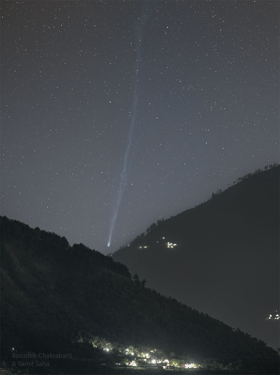 A starry sky is seen above two tree-covered mountains
that slope up on both sides of the image. In the central
valley the head of a comet is seen, with a long tail 
flowing nearly vertically upward toward the top of the 
tall frame. 
Więcej szczegółowych informacji w opisie poniżej.