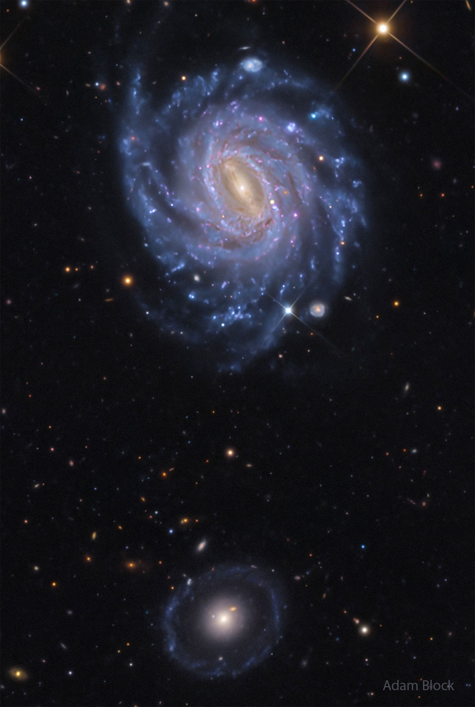 A starfield is shown showing two prominent galaxies. 
Near the top is a bright spiral galaxy with several blue
spiral arms. Near the bottom is a fainter circular 
galaxy with a bright center. 
Więcej szczegółowych informacji w opisie poniżej.