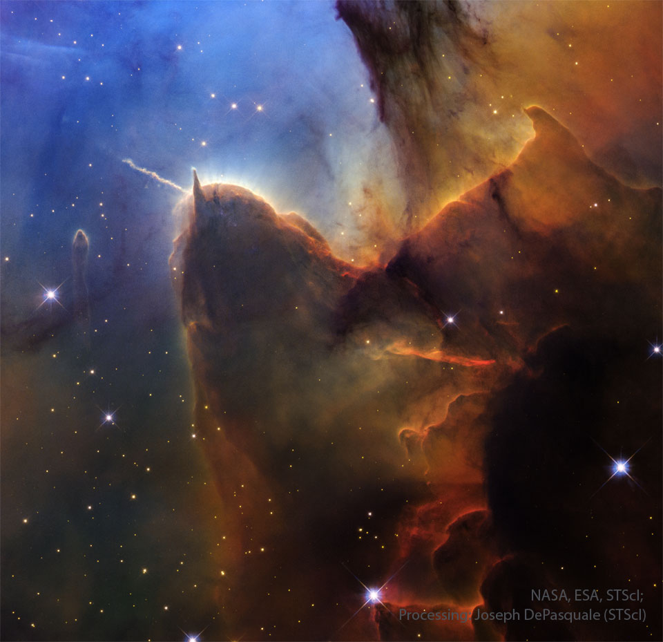A field of stars on the left is mirred by a wall of
opaque brown dust on the right. Jutting out from the wall is
a long pillar with a rounded end that has a prominent light-
colored jet emanating toward the upper left. The stellar 
background toward the upper left is dark blue.
Więcej szczegółowych informacji w opisie poniżej.