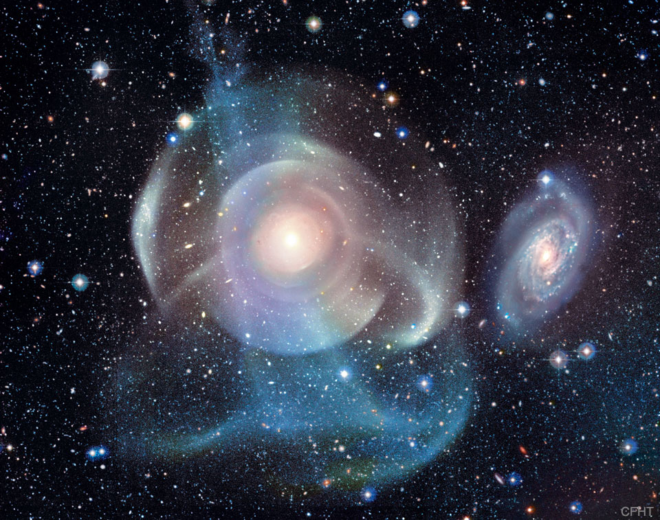 A starfield surrounds a complex background galaxy.
The galaxy center is surrounded by numerous shells, some
circular and concentric, but others colorful and 
filamentary. 
Więcej szczegółowych informacji w opisie poniżej.