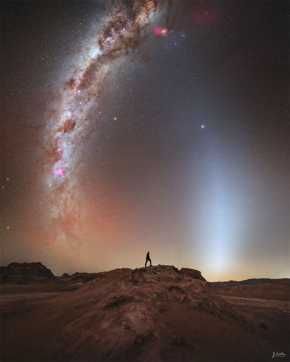 A distant person stands on a rocky landscape. Above is a
starry sky. Rising up from the horizon on either side of
the person are bright arching spires. 
Więcej szczegółowych informacji w opisie poniżej.