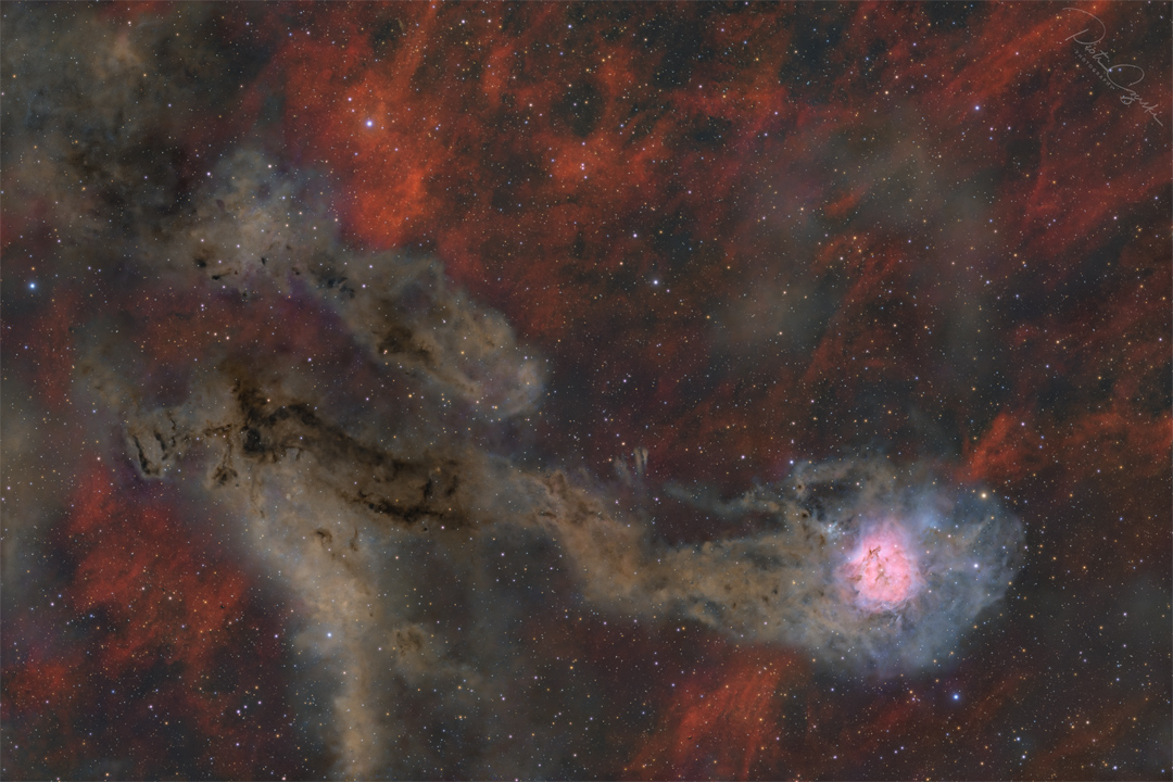 A starfield is shown against a patchy red-glowing
background. Two irregular brown trails occur, the lower
of which culminates in a bright pink and white region.
Więcej szczegółowych informacji w opisie poniżej.